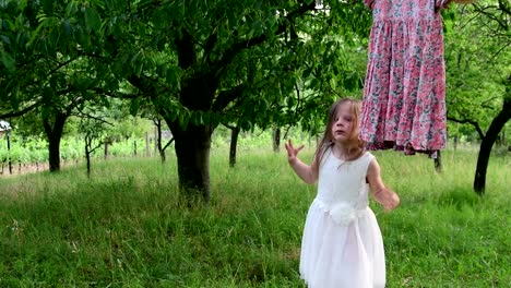 A-cute-girl-dances-in-the-natural-garden.-Little-girl-dances-and-jumps-on-a-small-trampoline.-Little-girl-wears-white-wedding-dress