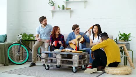 Glückliche-Freunde-haben-Partei-und-gemeinsam-zu-singen,-während-ihr-Freund-zu-Hause-Gitarre-spielen