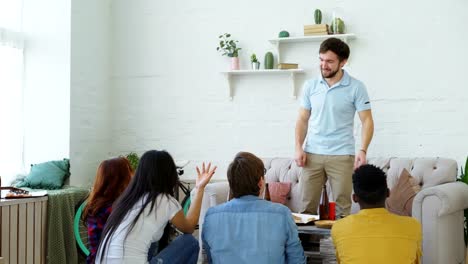 Group-of-friends-having-fun-playing-party-game-at-home.-Young-guy-showing-something-or-somebody-and-his-flatmates-trying-to-guess-it