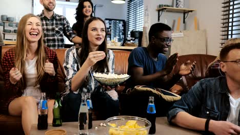 Grupo-de-origen-étnico-mixto-viendo-el-juego-de-deportes-en-la-televisión.-Cerca-de-los-fanáticos-emocionales-en-sofá-con-bebidas-y-aperitivos-4K-lenta