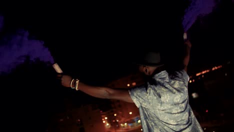 Young-man-celebrating-with-smoke-bombs-on-urban-rooftop