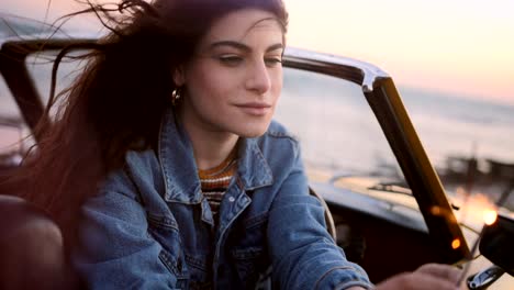 Woman-in-convertible-car-holding-sparklers-at-beach-at-sunset