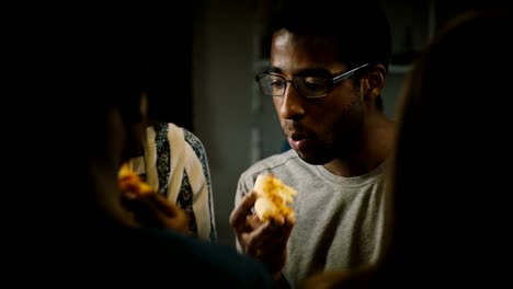 Pizza-de-afroamericano-joven-comiendo-en-una-fiesta-informal.-Los-jóvenes-disfrutan-de-comida-rápida-en-la-cocina-en-casa