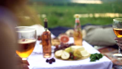 Young-happy-friends,-laughing-and-drinking-wine-at-a-picnic,-at-sunset-overlooking-the-mountains