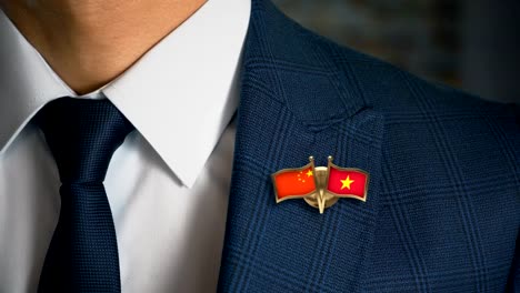 Businessman-Walking-Towards-Camera-With-Friend-Country-Flags-Pin-China---Vietnam