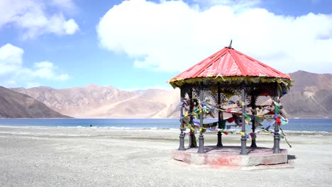 Roter-Pavillon-in-Bergen-und-Pangong-Tso-(See)-und-Gebetsfahnen-flattern-im-Wind.-Es-ist-riesig-und-höchste-See-in-Ladakh-und-blauer-Himmel-im-Hintergrund,-es-erstreckt-sich-von-Indien-nach-Tibet.-Leh,-Ladakh