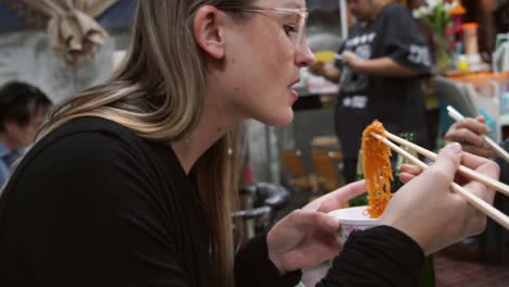 slow-motion-young-woman-in-glasses-enjoying-noodles-with-chopsticks-at-a-casual-restaurant