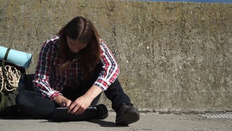 Man-tourist-backpacker-sitting-with-tablet-on-wall-outdoor-4K