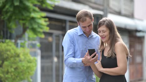 Young-happy-couple-using-phone-together-outdoors