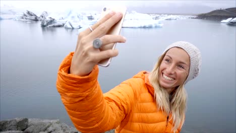 Retrato-de-selfie-de-vídeo-lenta-de-mujer-joven-de-pie-junto-a-la-laguna-glaciar-en-Islandia