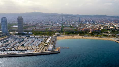 Flying-along-Barcelona-shore-with-city-skyline,-Spain.-Aerial-view