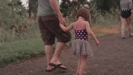 A-little-girl-and-her-dad-walk-hand-in-hand-down-a-park-trail