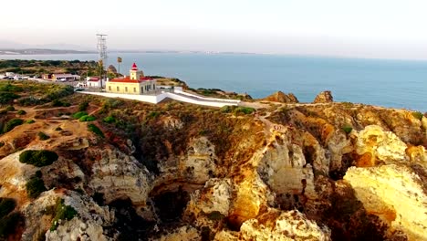 Faro-de-Ponta-da-Piedade-en-acantilado-junto-al-mar-en-vista-aérea-de-la-puesta-del-sol,-Lagos,