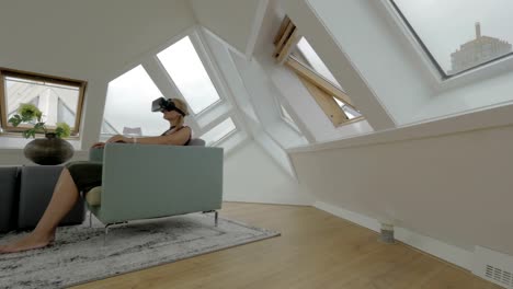 Blick-auf-junge,-blonde-Frau-sitzt-auf-der-Seite-der-Sessel-mit-Tablet-im-inneren-Raum-in-einem-Cube-Haus.-Rotterdam,-Niederlande