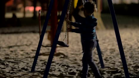 Niños-divirtiéndose-con-columpios-vacíos-en-el-patio-en-la-noche