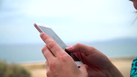 Joven-mujer-bonita-en-vestido-con-smartphone-sentado-en-el-paseo-marítimo-de-la-ciudad