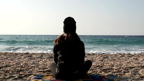 Mädchen-sitzt-auf-dem-Strand-des-Mittelmeers-an-einem-kühlen-Herbsttag.