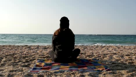 Mädchen-sitzt-auf-dem-Strand-des-Mittelmeers-an-einem-kühlen-Herbsttag.