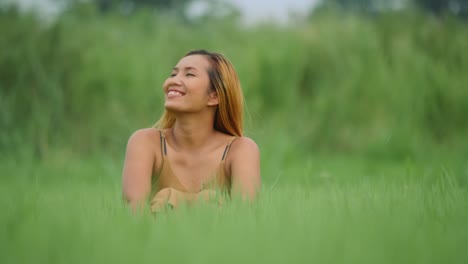 Mujer-relajante-sentarse-con-los-brazos-alzados-en-el-campo-de-hierba