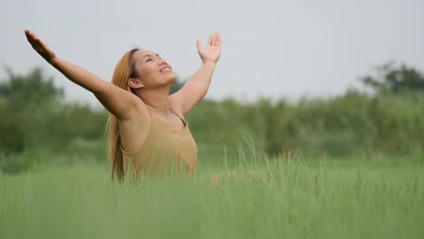 Joyful-Woman-Sitting-on-the-green-field-and-raising-her-hand-refresh-life