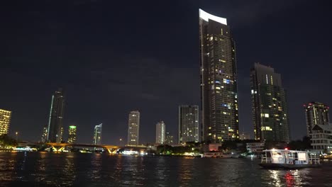 edificios-corporativos-en-la-orilla-del-río-con-oficinas.-tiempo-de-la-noche-en-la-gran-ciudad,-centros-de-luz-desde-las-ventanas-de-negocios