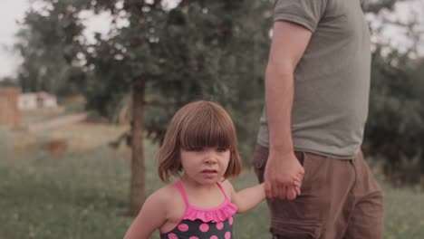 A-little-girl-and-her-dad-walk-hand-in-hand-down-a-park-trail