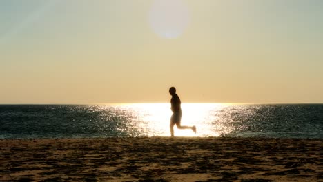 männlichläufer-läuft-am-Strand,-Sonnenuntergang-Silhouette,-Zeitlupe