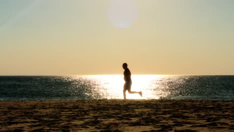 corredor-masculino-corriendo-en-la-playa,-silueta-de-la-puesta-de-sol,-cámara-lenta