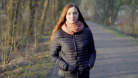 Junge-attraktive-Frau-mit-roten-langen-Haaren,-die-zu-Fuß-in-den-Park-bei-Sonnenuntergang