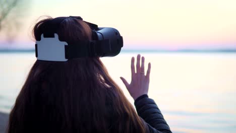 Attraktive-weiße-Frau-nutzt-virtual-Reality-Brille-am-See-bei-Sonnenuntergang