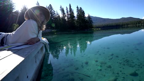 Woman-lying-down-on-wooden-pier-above-stunning-lake-touches-the-surface-of-crystal-clear-water