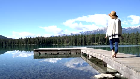 Woman-walking-over-pier-standing-above-stunning-mountain-lake-in-the-Canadian-rockies