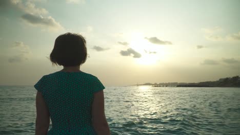 Frau-in-kurzen-grünen-Kleid-Wanderer-auf-nassen-Felsen-mit-plätschernden-Wasser-des-Meeres-in-der-Sonne.-Auf-den-Sonnenuntergang