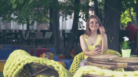 beautiful-girl-in-the-Park-sitting-at-a-table-with-a-smartphone