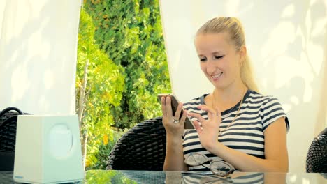 Hermosa-rubia-corresponden-con-amigos-en-el-teléfono-inteligente-en-café-de-verano.