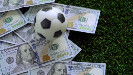 Fußball-Business,-Fußball-spielen-Konzept:-ein-Fußball-Fallenlassen-auf-US-Dollarnoten,-die-über-grünen-Rasen-verteilt.-Slow-Motion-VDO.