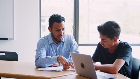 Tutor-de-secundaria-dando-uno-a-uno-matrícula-de-estudiante-masculino-en-el-escritorio