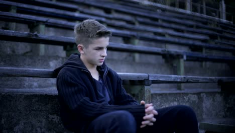 Boy-sitting-on-stadium-tribune,-devastation-and-poverty-around,-city-after-war