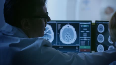 Control-Room-Arzt-und-Radiologen-besprechen-Diagnose-beim-beobachten-Verfahren-und-Monitore-zeigen-Gehirnscans-Ergebnisse,-In-den-Hintergrund-Patient-erfährt-MRT-oder-CT-Scan.