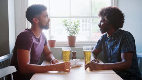 Mezclado-raza-joven-y-su-padre-negro-bebiendo-cerveza-y-hablando-en-una-mesa-en-un-bar,-cerrar,-vista-lateral