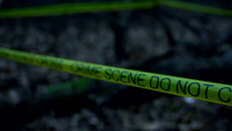 Closeup-of-yellow-crime-scene-tape-in-the-woods,-forensic-expert-working-at-site