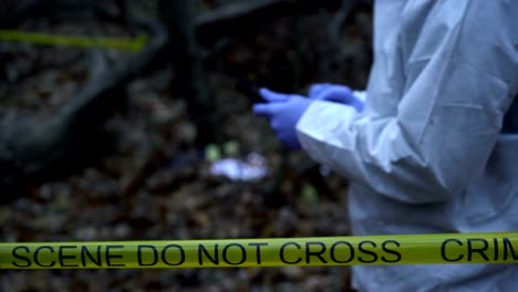 Crime-lab-field-worker-entering-data-on-tablet-at-crime-scene-in-forest