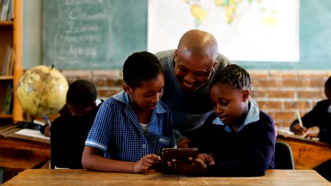 Male-teacher-using-digital-tablet-with-students-in-classroom-4k