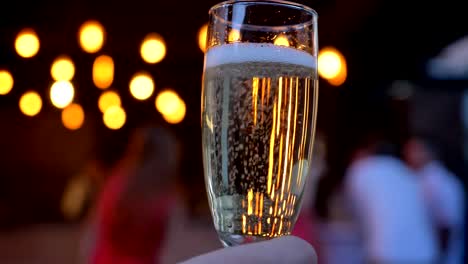 Glass-of-sparkling-champagne,-flickering-lights-in-the-background,-party,-bokeh