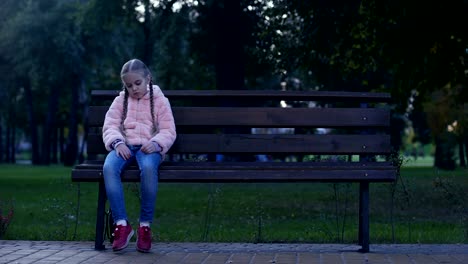 Sad-school-girl-sitting-on-bench-in-park,-lost-missing-kid,-waiting-for-parents