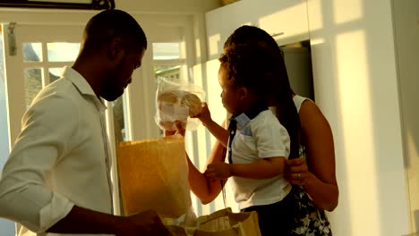 Side-view-of-young-black-mother-and-son-looking-in-grocery-bag-in-kitchen-of-comfortable-home-4k