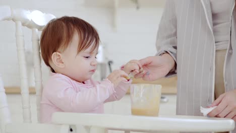 Cute-baby-girl-refusing-to-eat-fruit-puree,-but-her-patient-mother-managing-to-feed-her-with-spoon