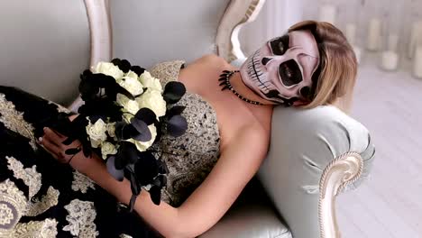 A-creepy-woman-with-makeup-in-the-form-of-a-skull-lies-on-a-retro-sofa.Halloween