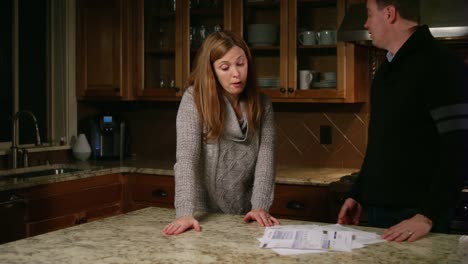 Husband-and-wife-looking-at-bills-in-the-kitchen,-stressed-and-frustrated