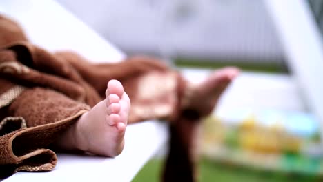 close-up-of-children's-legs,-a-little-one-year-old-girl-wrapped-in-a-towel,-swinging-on-a-swing-in-the-garden,-in-the-summer